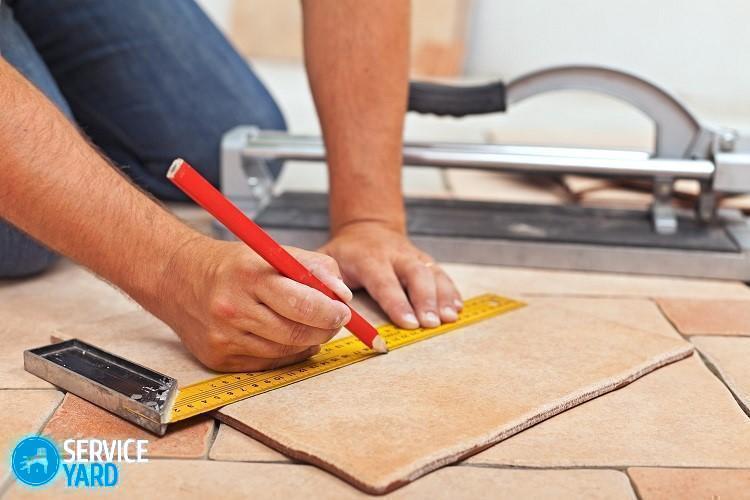 Pose de carreaux de sol en céramique - mains d'homme marquant le carreau à couper, gros plan
